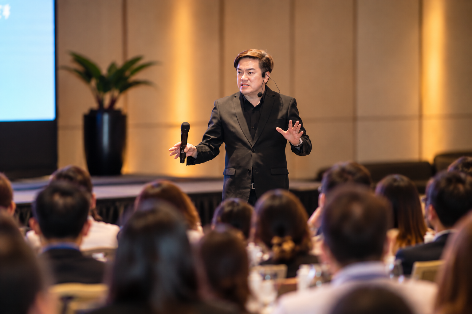 Coach AJ speaking on stage with a microphone at a corporate event