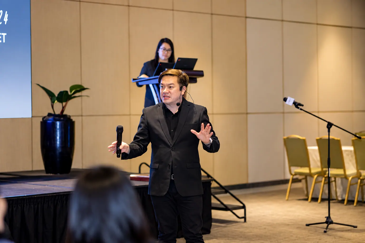 Coach AJ speaking on stage with a microphone at a corporate event